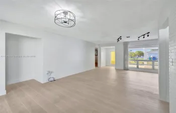 The bright and airy living area showcases fresh paint, modern lighting, and elegant wood-look tile flooring, creating a stylish and inviting space filled with natural light.