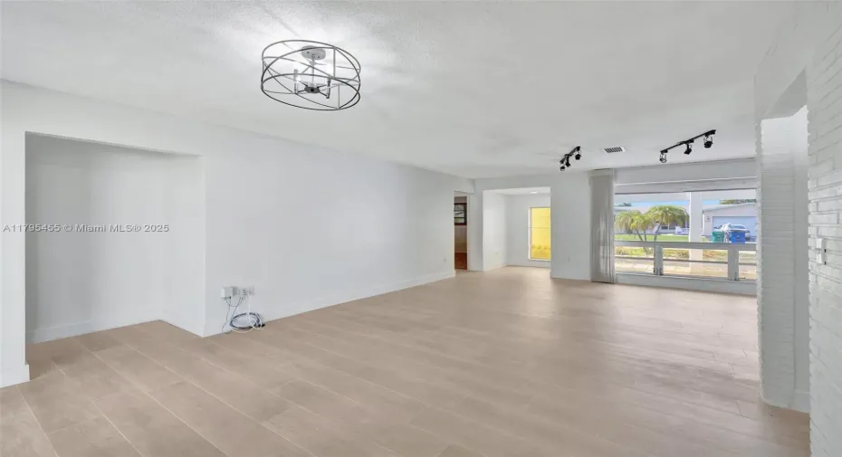The bright and airy living area showcases fresh paint, modern lighting, and elegant wood-look tile flooring, creating a stylish and inviting space filled with natural light.