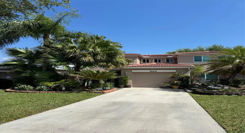 Welcome to this stunning home, featuring a beautifully landscaped front yard with lush tropical foliage and towering palm trees.